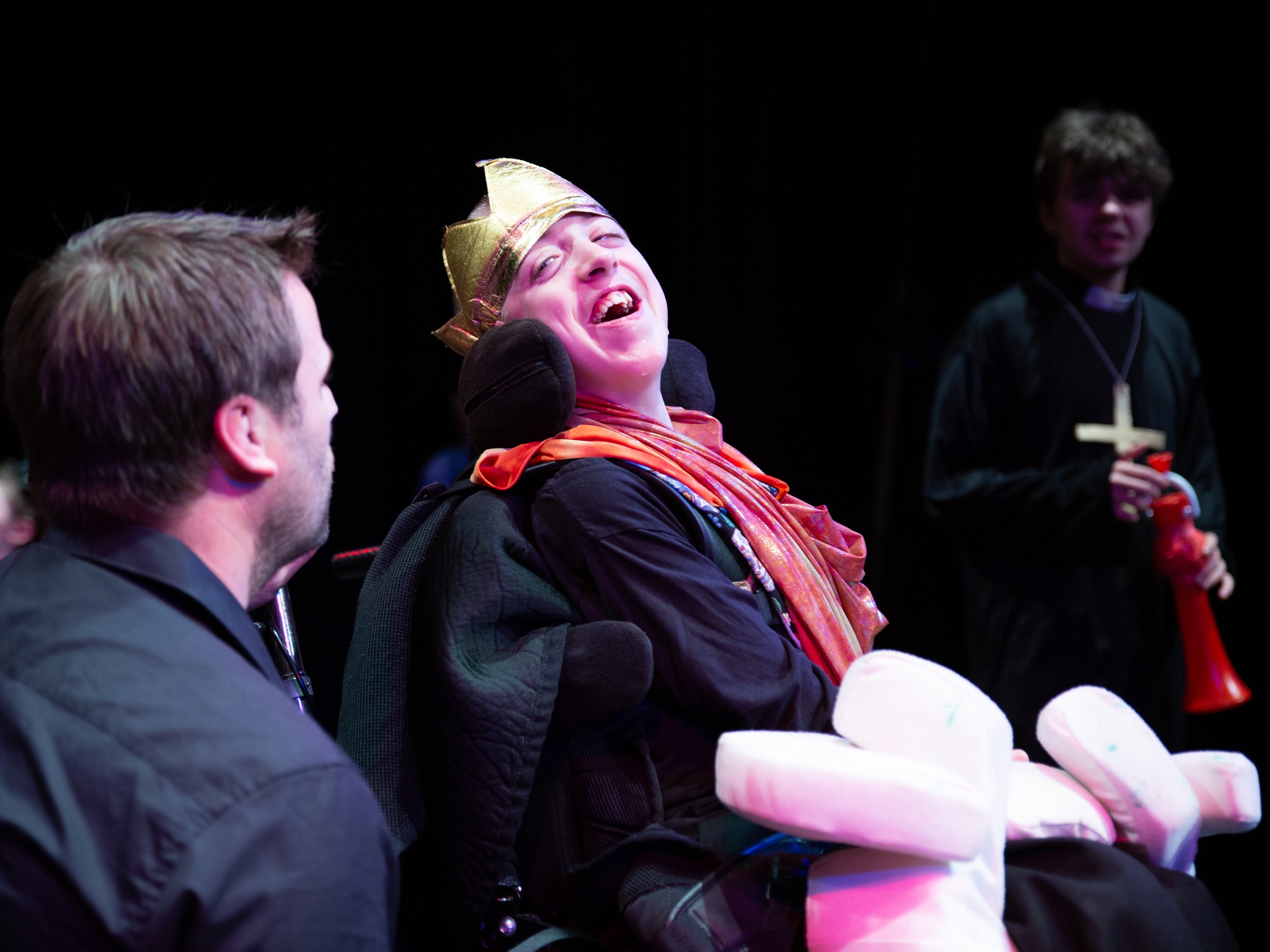 Child using a wheelchair smiles on a theatre stage.