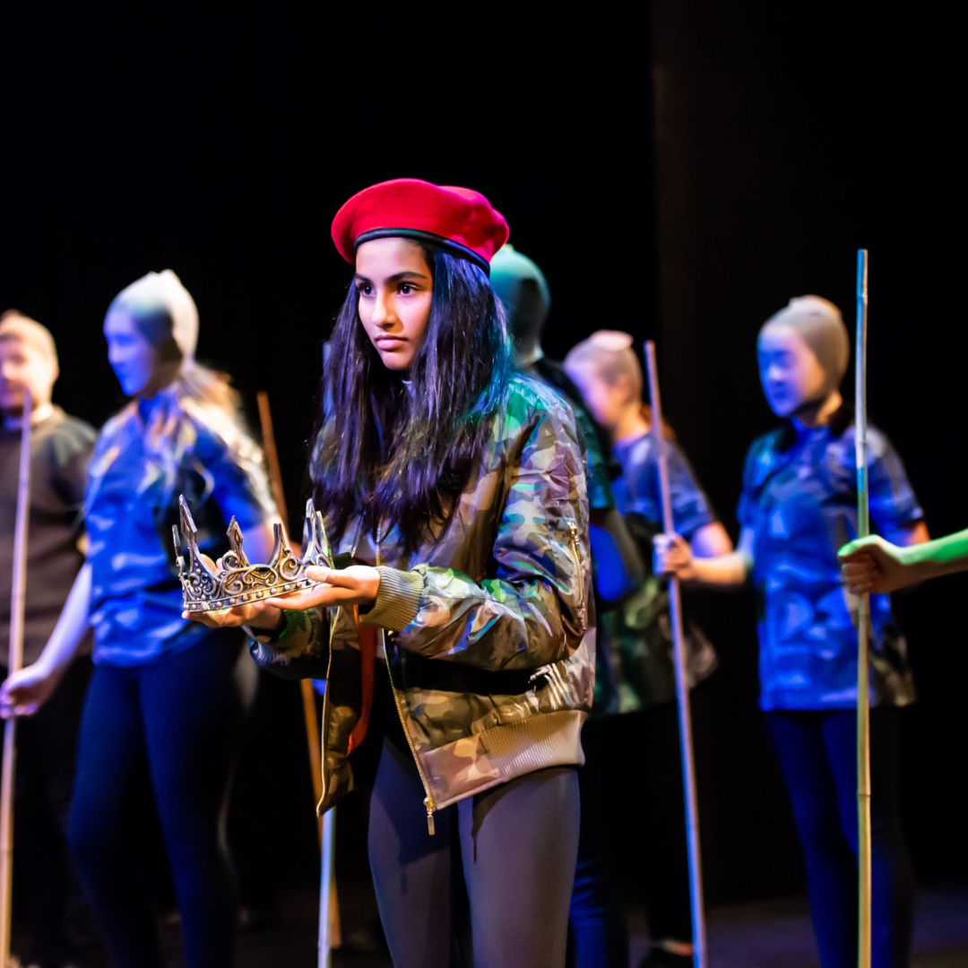 A girl on stage in a soldier's uniform holding a crown