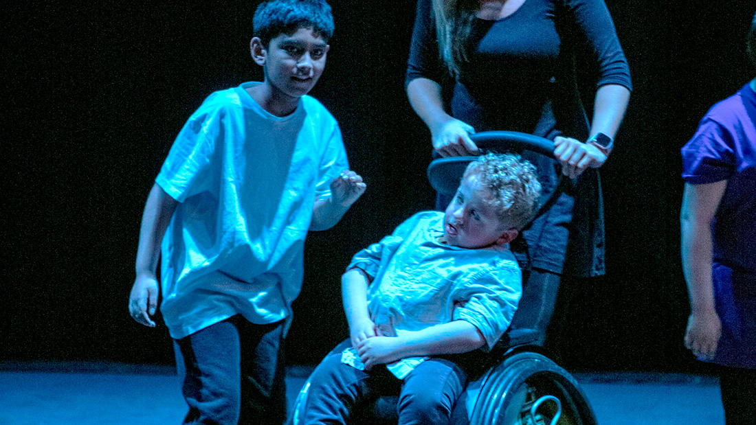 Two students - one using a wheelchair - perform on a theatre stage.