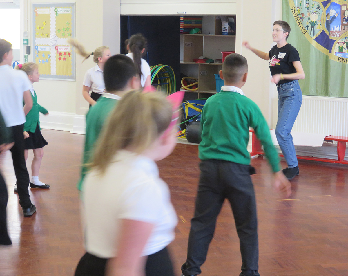 Primary school children taking part in a workshop, with a Coram Shakespeare Schools Foundation facilitator at the front of the class.